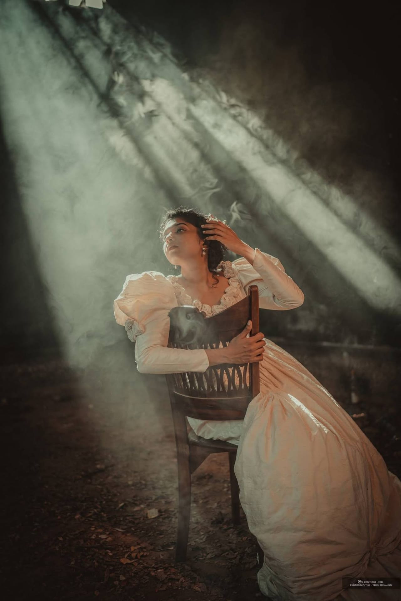 A bride in an old-fashioned gown lit by shafts of light through a derelict roof