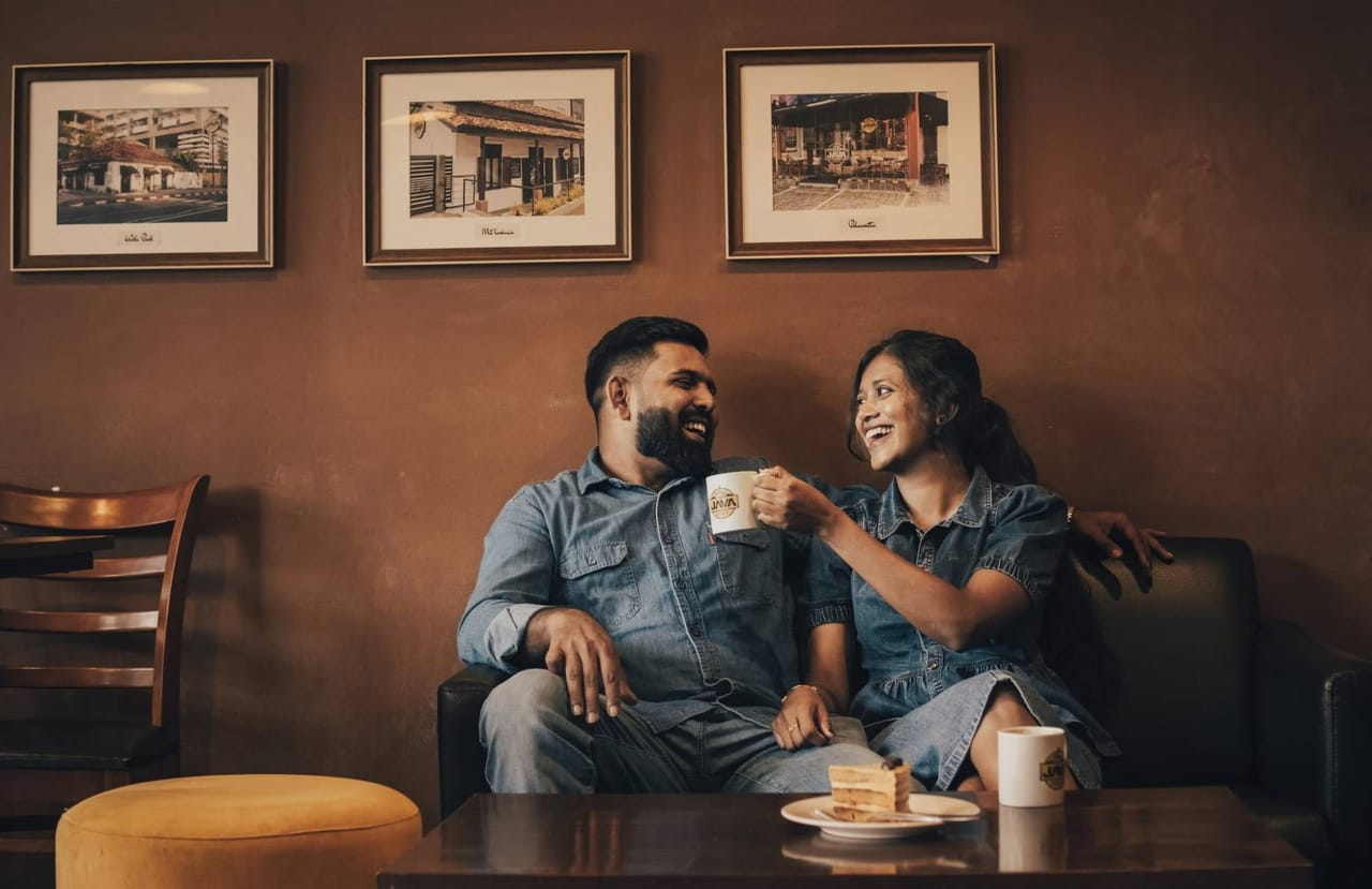 A couple in denim laughing together over coffee on a café sofa in Kandy