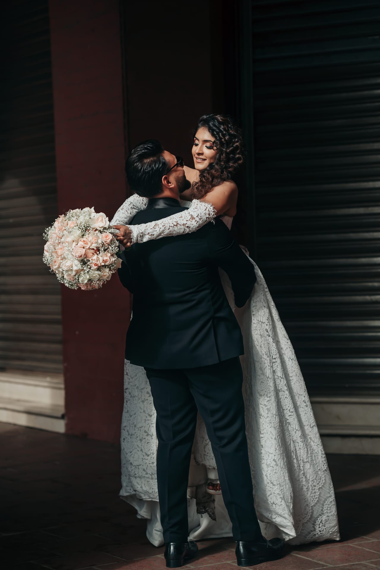 A groom lifting his bride in her white gown against a dark shuttered doorway