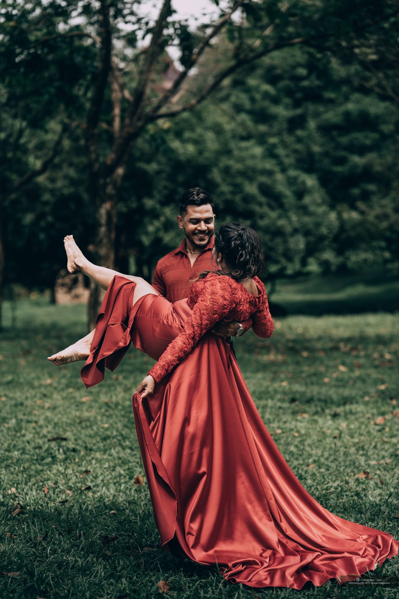 A man carrying a woman in a long red dress across a dark lawn