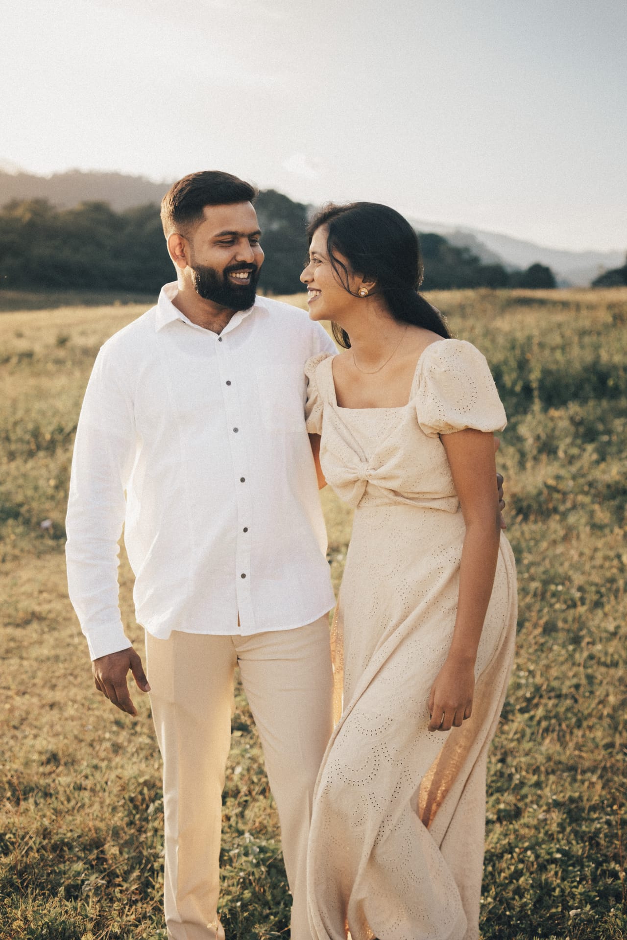 A couple in cream clothes walking through a golden field at the end of the day