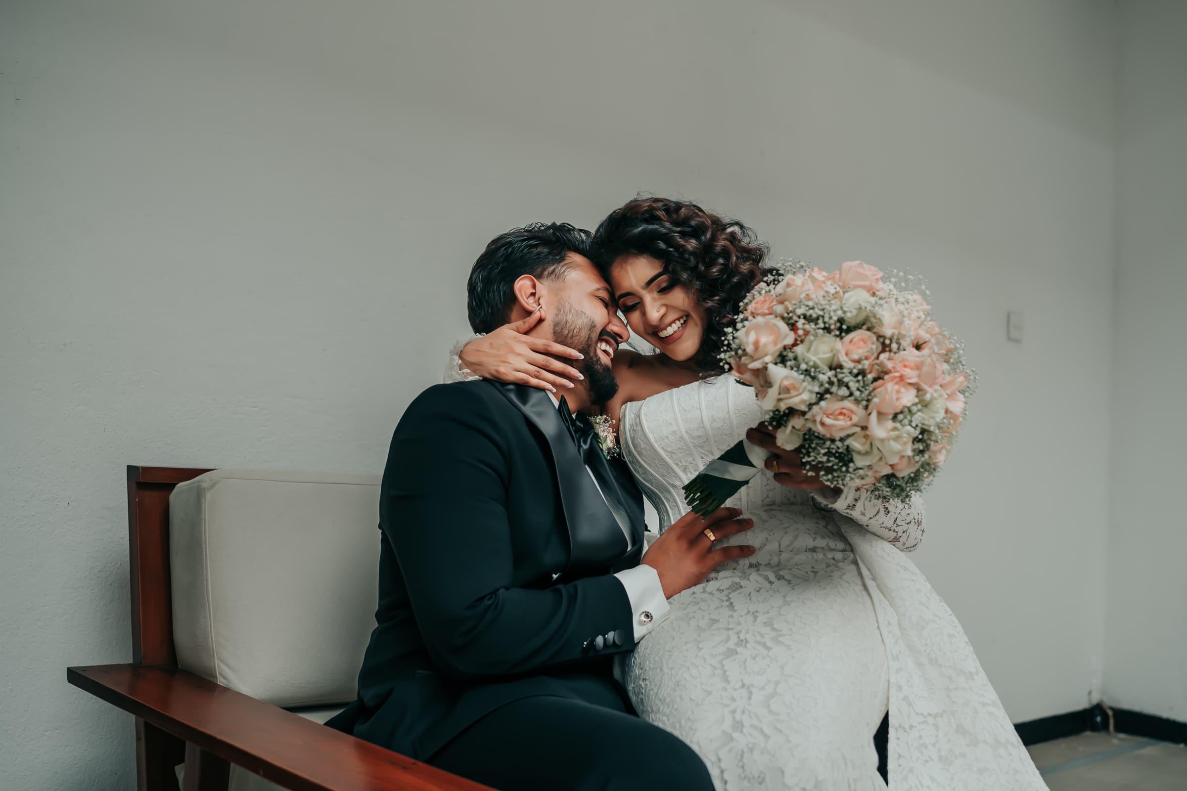 A bride and groom laughing together, her bouquet between them