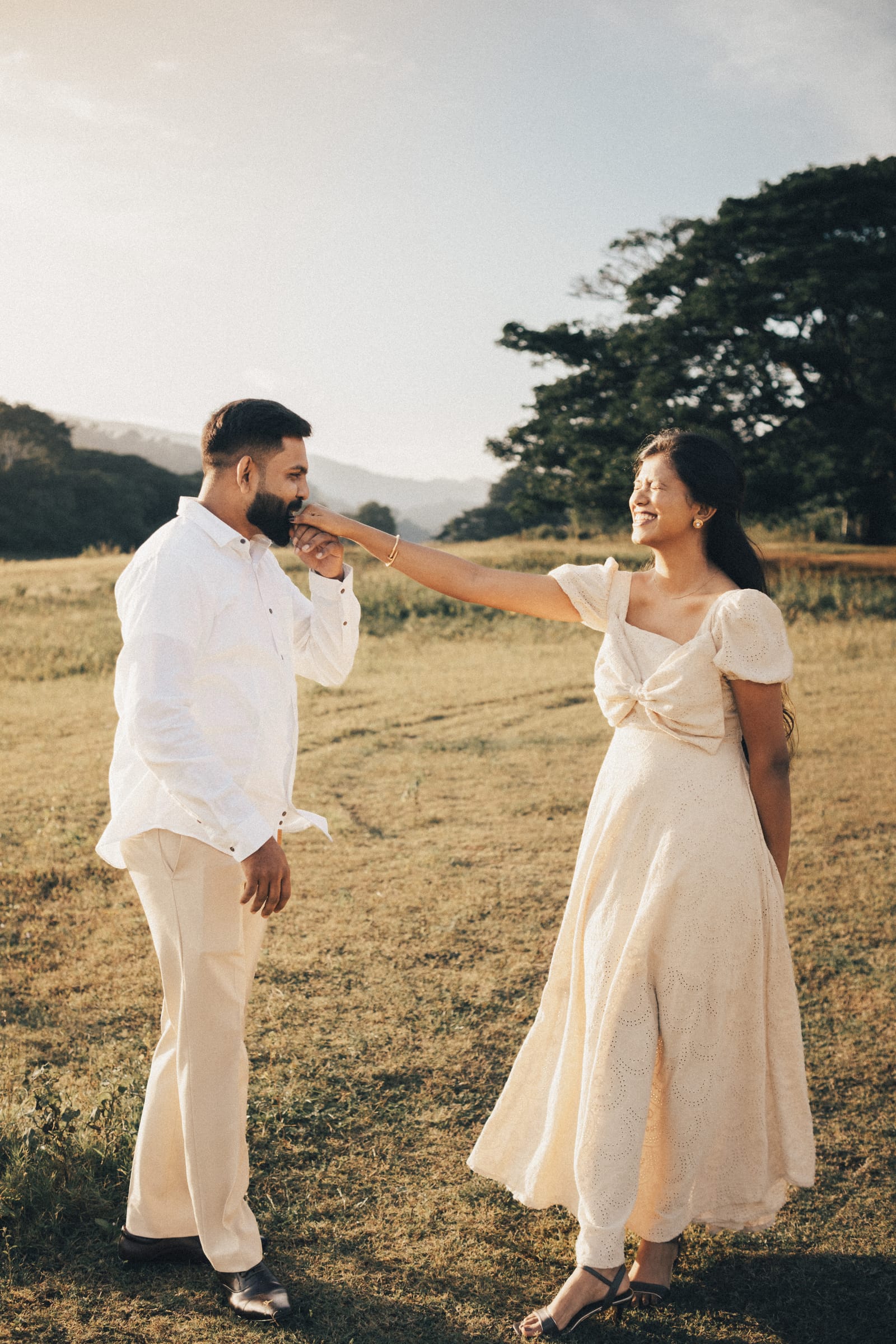 A groom kissing his bride's hand in a golden field with the hills behind them