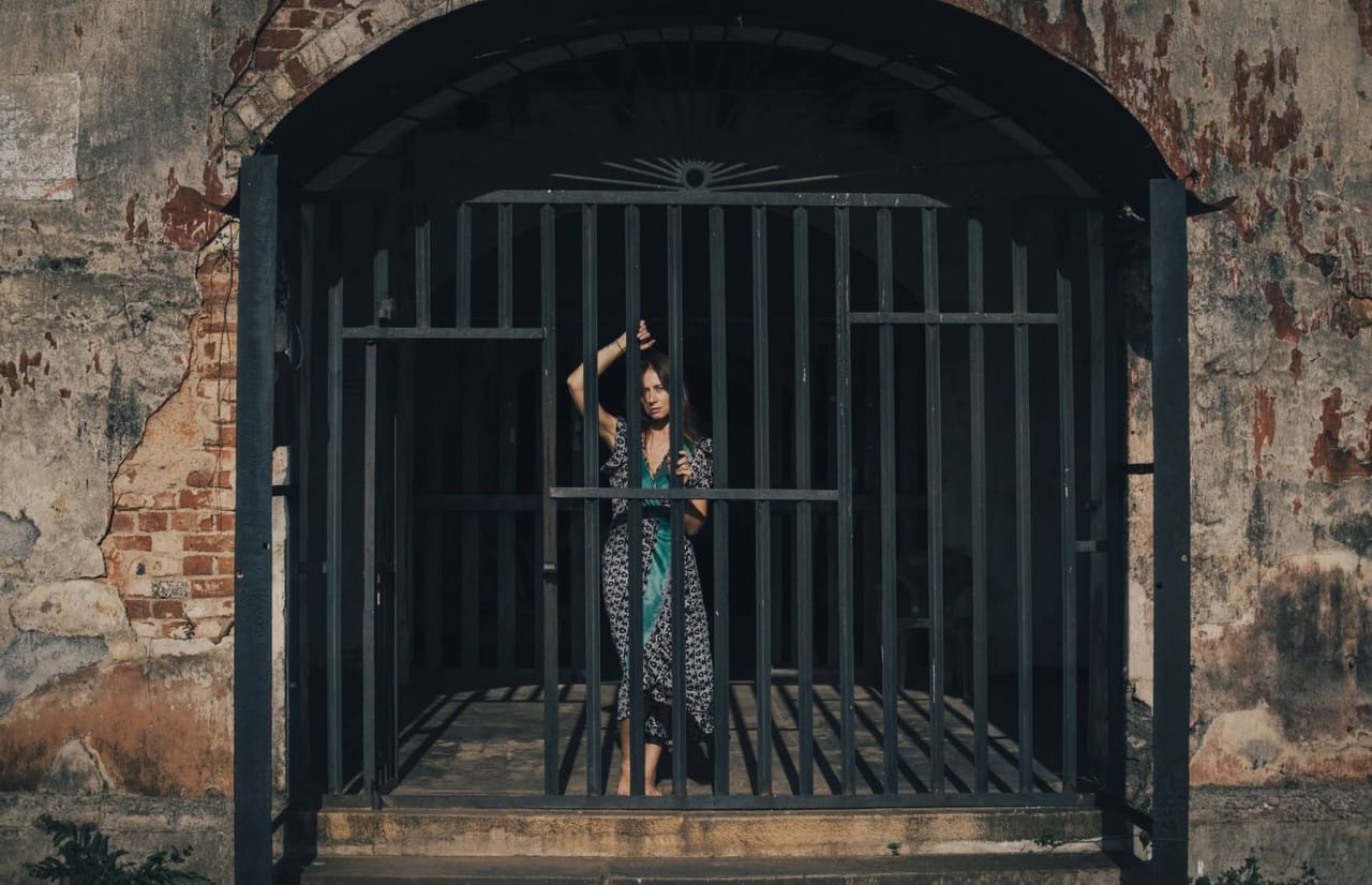 A woman standing behind the iron gate of a weathered Galle Fort building