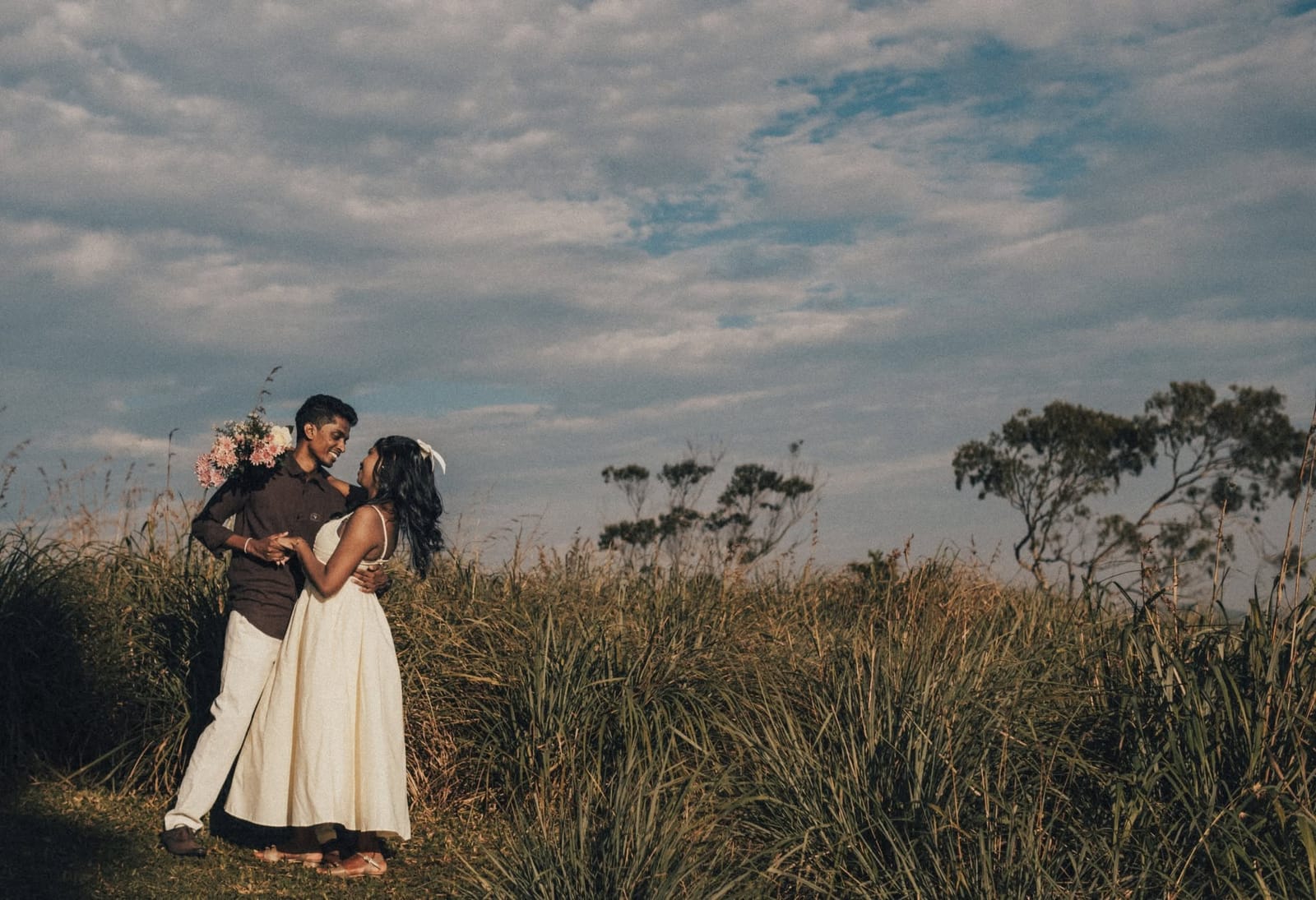 A couple holding each other in a field of long grass under a dusk sky