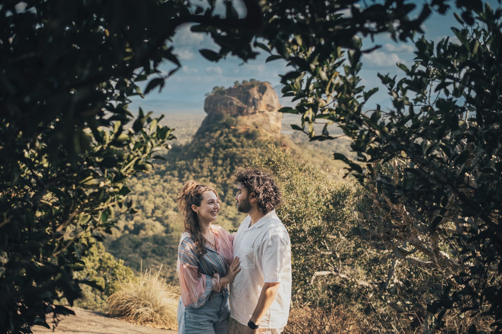 Lousa and Shamil laughing together, framed by leaves, with Sigiriya rock behind them
