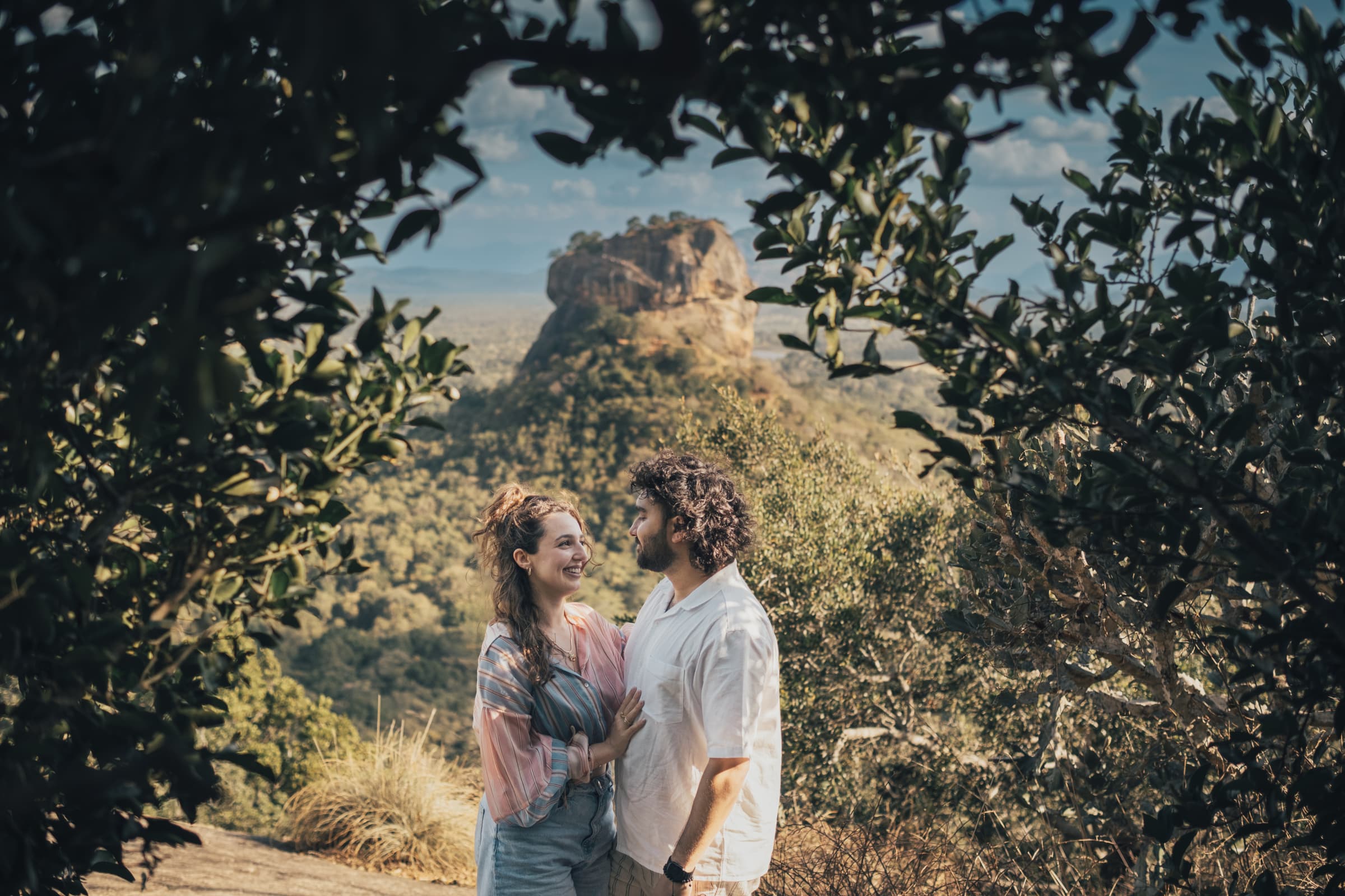 Lousa and Shamil laughing together, framed by leaves, with Sigiriya rock behind them