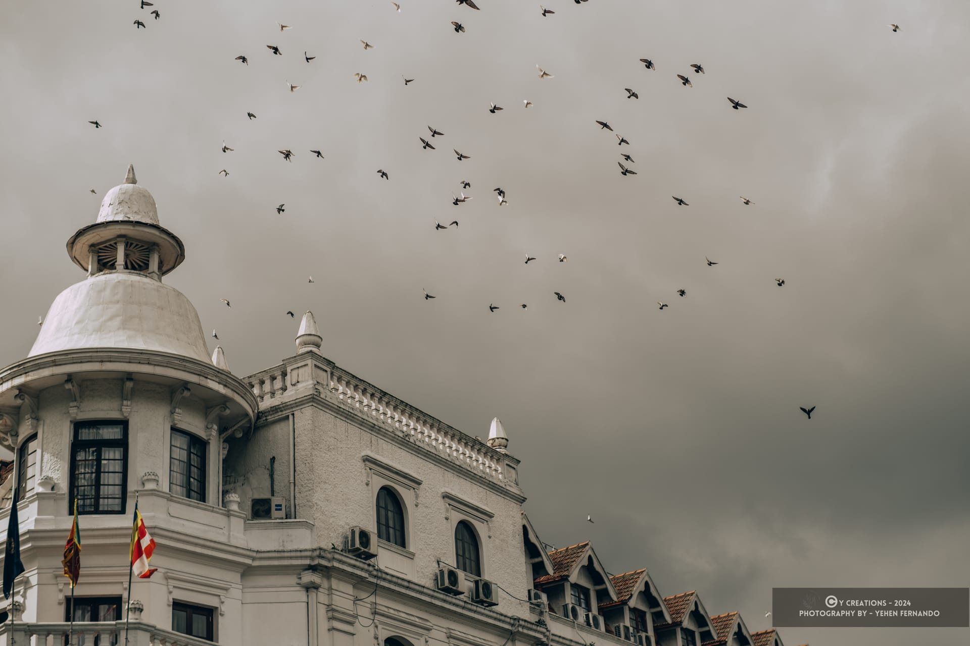 Birds circling above the rooftops and colonial towers of Kandy under a grey sky