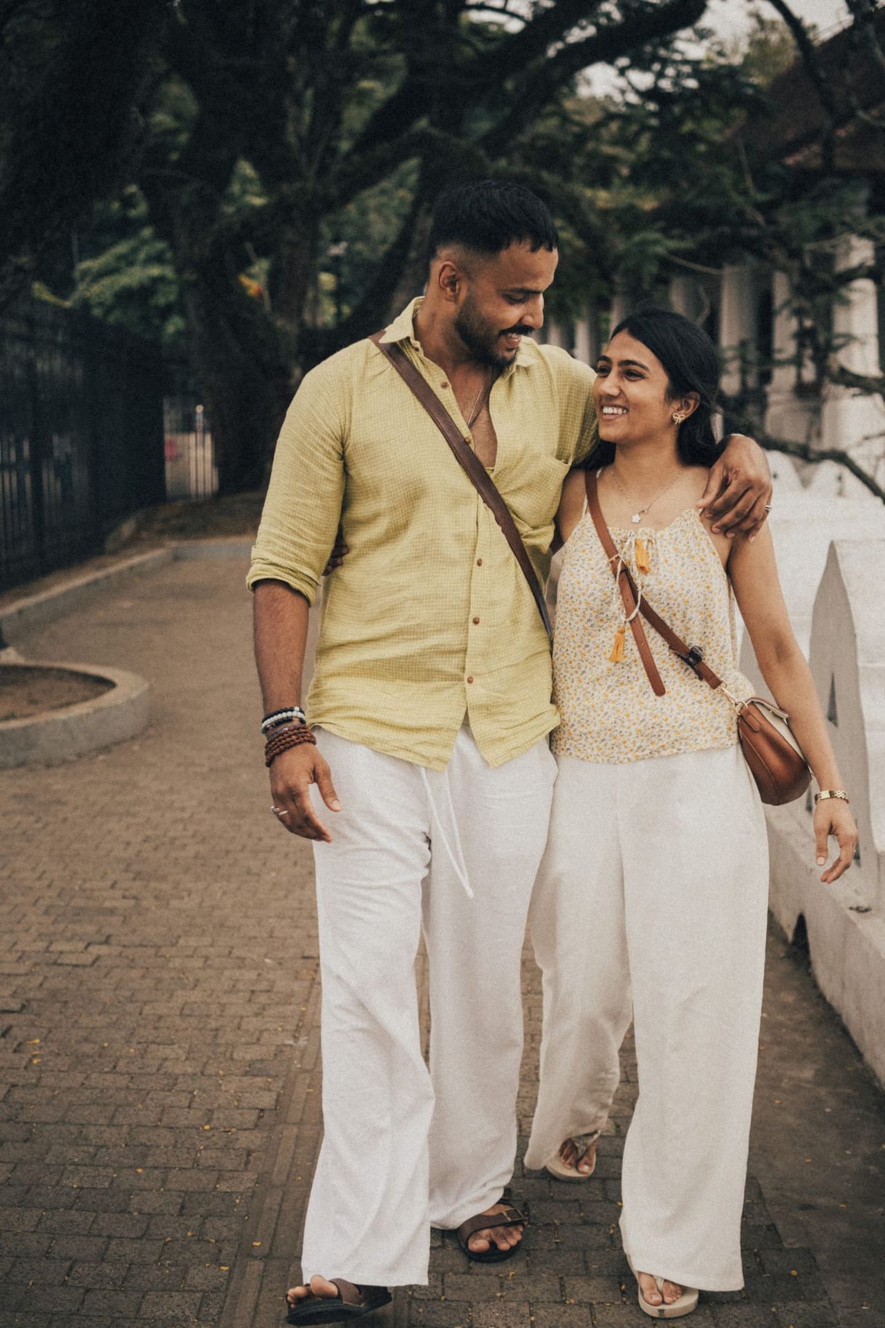 A couple walking arm in arm along a tree-lined path beside Kandy Lake