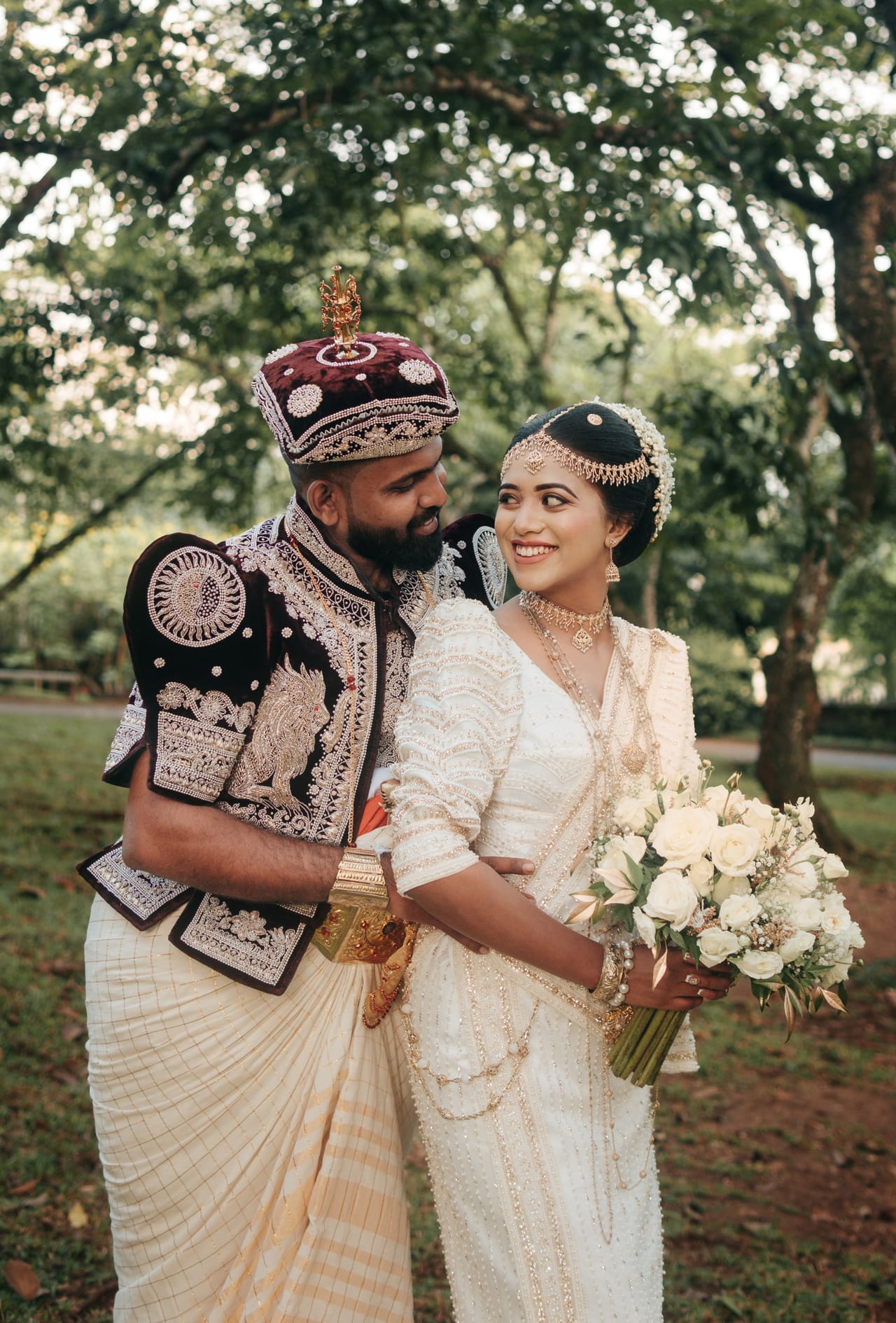 A groom in traditional Kandyan nilame dress standing with his bride and her bouquet