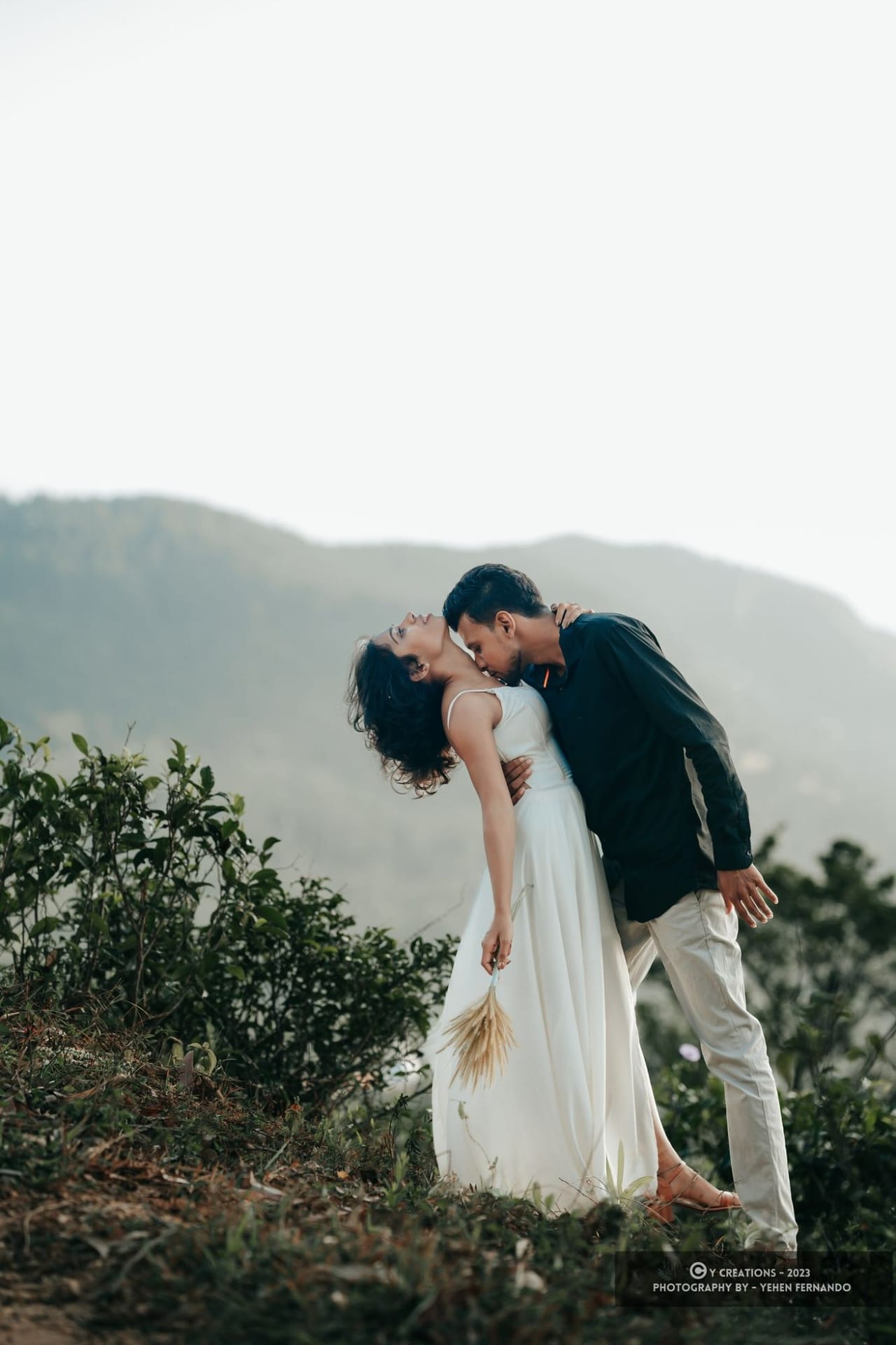 A couple on a hillside above the tea country, the hills fading into mist behind them
