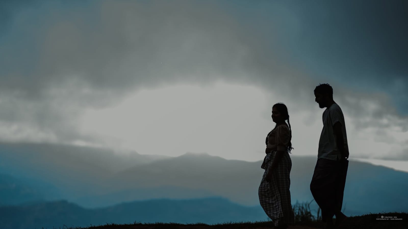 A couple standing together in silhouette against the hills at dusk