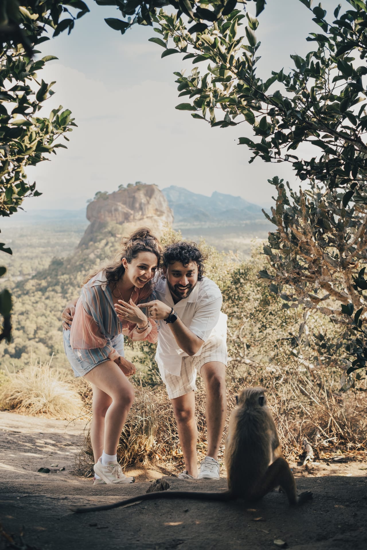 A couple laughing together on a rock with Sigiriya in the distance