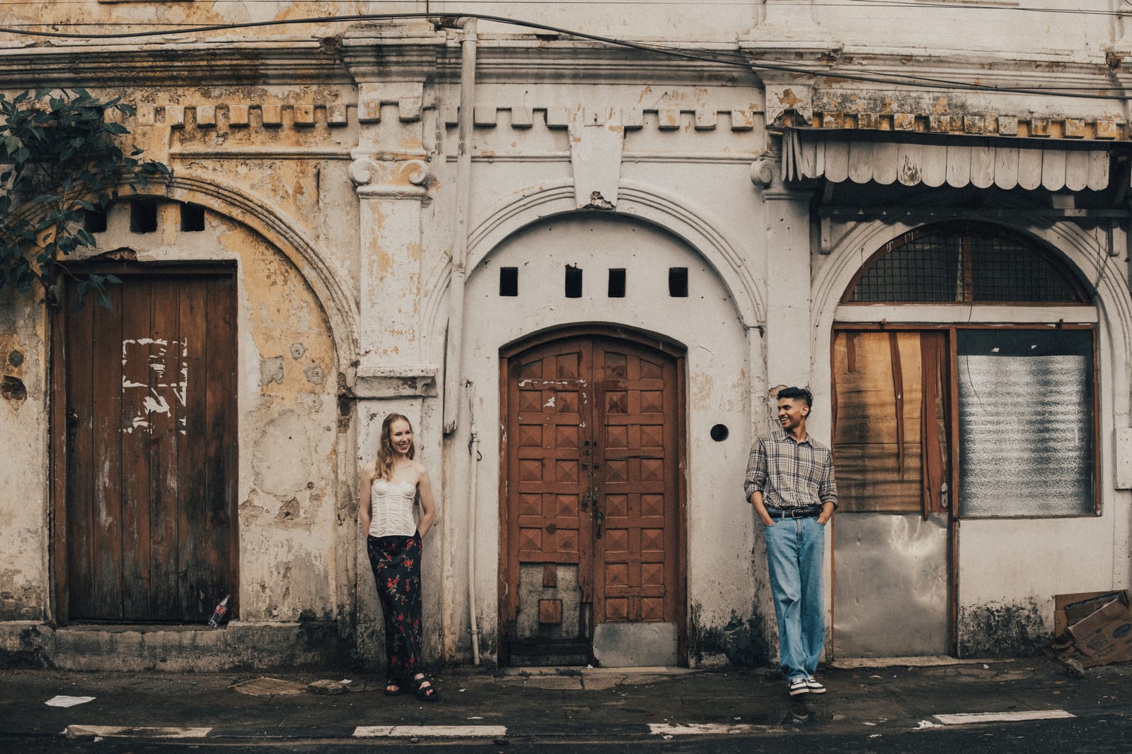 A couple standing apart against the weathered doorways of an old colonial street