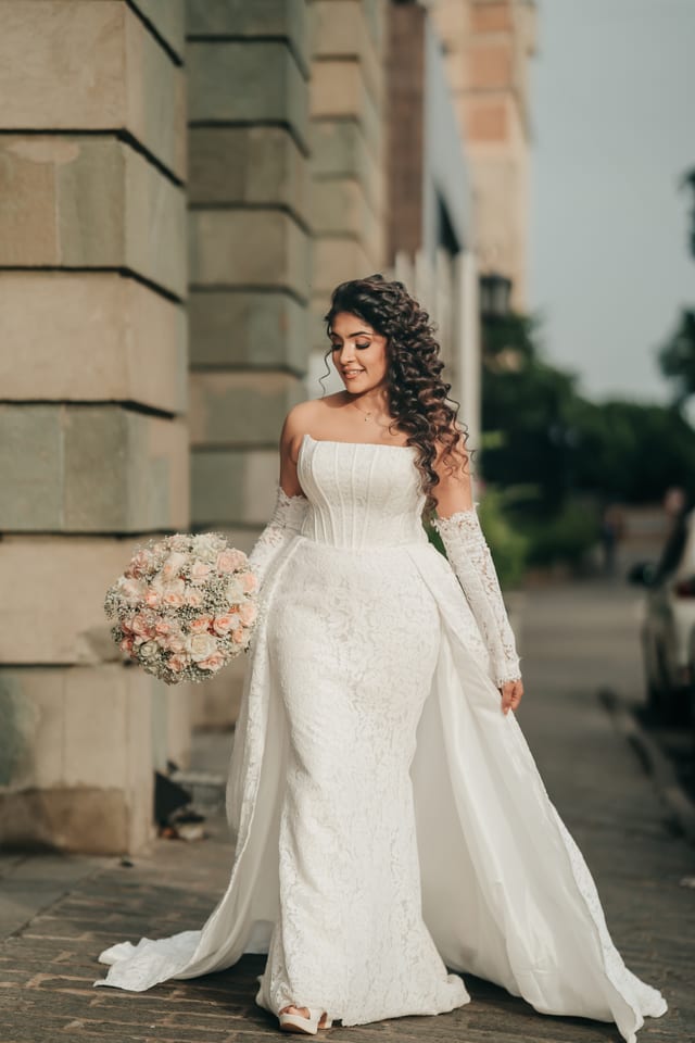 A bride in a white gown holding her bouquet on a quiet street